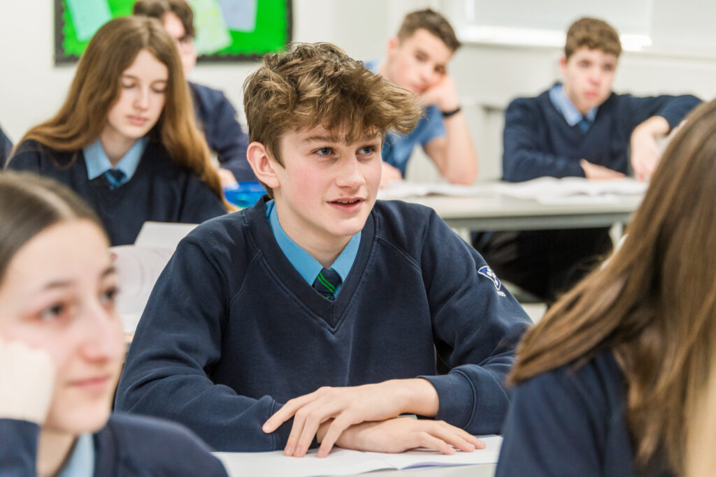 A male student smiling and listening in a classroom with other students